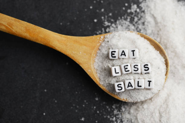 Eat less salt advice written with plastic letter beads on granulated salt – healthy food lifestyle stock photo