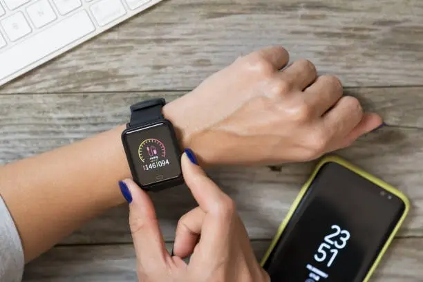 Woman measuring blood pressure with modern smart watch against wooden table