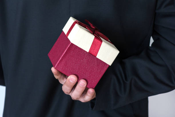 istock Man in suit holding red rose gift box behind his back 1126742800