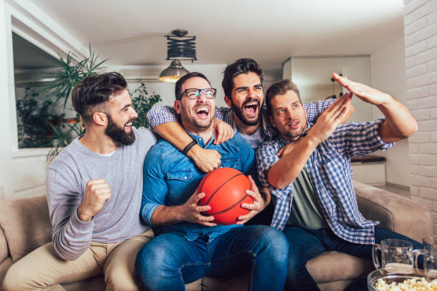 счастливые друзья или любители баскетбола смотрят баскетбольный матч по телевизору и празднуют победу дома. концепция дружбы, спорта и раз - home interior entertainment sofa men стоковые фото и изображения