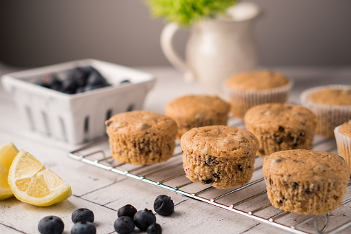 Fresh baked whole wheat lemon-blueberry muffins. Muffins cooling on a wire rack. Fresh blueberries and lemons on the table.