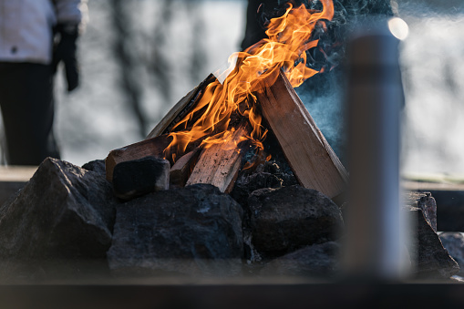A thermos standing on a bench in front of a burning campfire​ during wintertime. Two women out of focus are in the background.