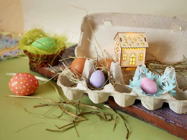 istock Fresh and Easter painted chicken and quail eggs in a packing tray, a toy house with illumination on a green table 1126782735