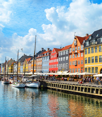 People walking at sunny Nyhavn embankment with moored boats, Copenhagen, Denmark