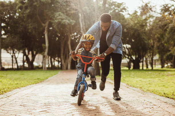 padre insegna a suo figlio in bicicletta al parco - figlio maschio immagine foto e immagini stock