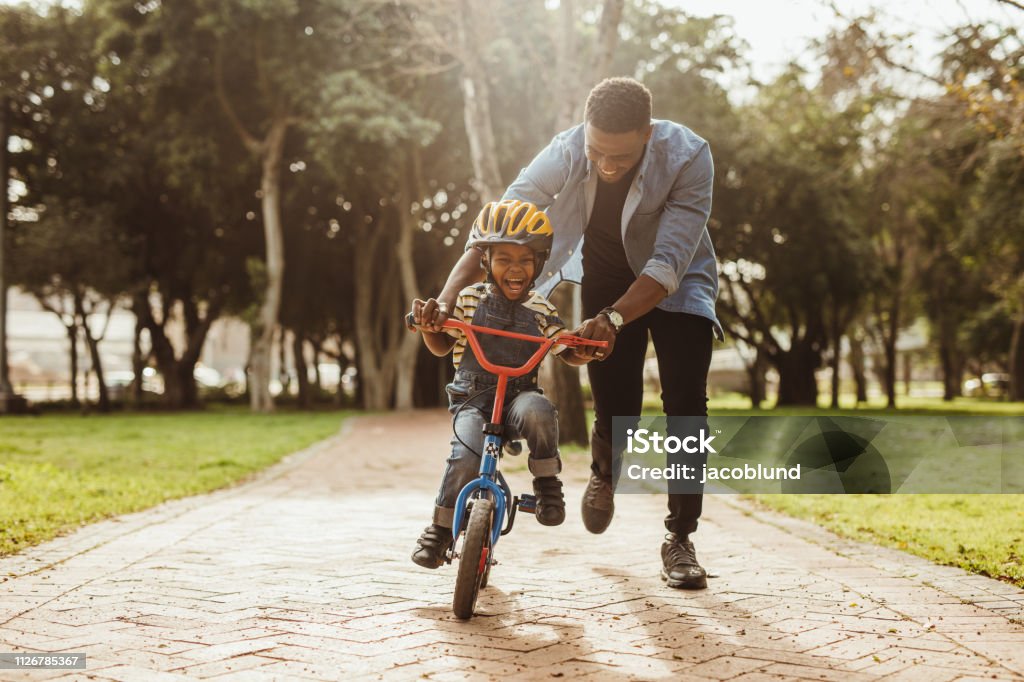 Father teaching his son cycling at park Boy learning to ride a bicycle with his father in park. Father teaching his son cycling at park. Child Stock Photo