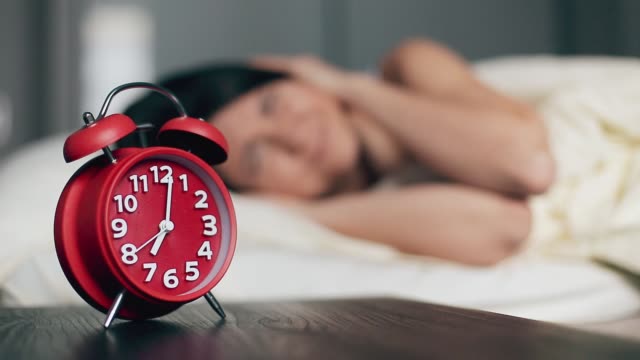Young woman switches off the alarm clock on the bed in the morning