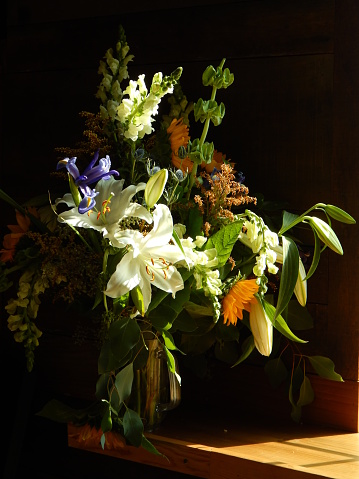 A still life of beautiful assorted springtime flowers in a glass vase sitting on a wooden table  exposed to bright sunlight.