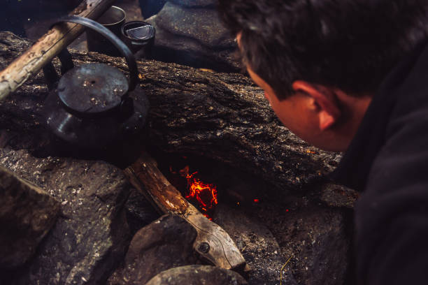 How to make fire. Tourist kindles bonfire. Traveler is lighting fire in camp. Man makes campfire in twilight. Active outdoor recreation. Camping in dusk. Active rest into wild. Man blowing on coals.