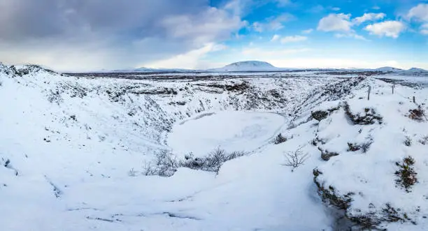 Panoramic view of the Kerid Volcano with snow and ice in the volcanic crater lake in Winter under a clear blue sky. located in the GrÃ­msnes area in south Iceland, along the Golden Circle route.