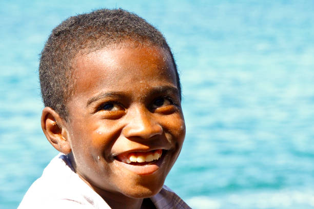Rear view of a cute little African boy peeing into the ocean during a trip to the beach in the summertime