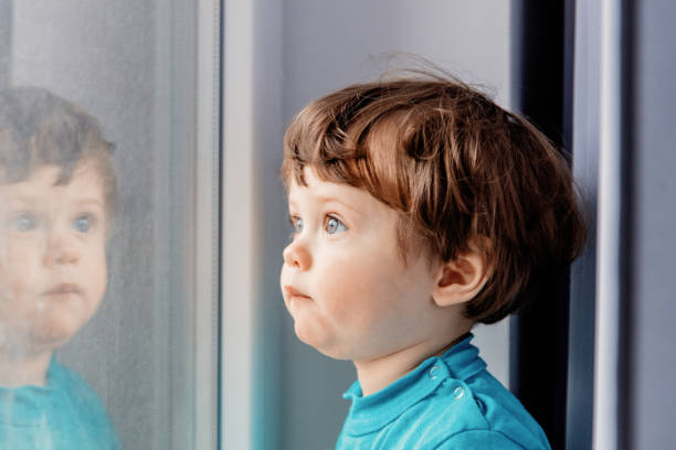 istock boy is standing by the window and looking into it 1126810127