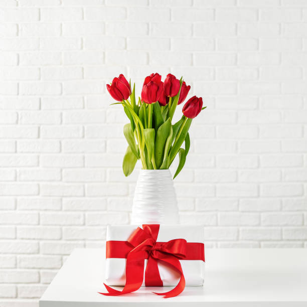 istock red tulips in white vase with gift box with red ribbon 1126816377