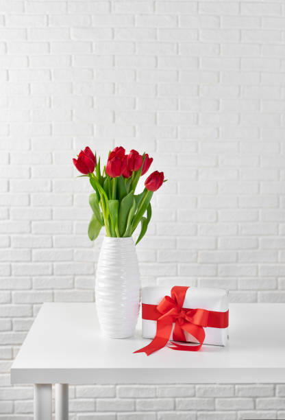 istock Red tulips in white vase next to a gift box with red ribbon 1126816379