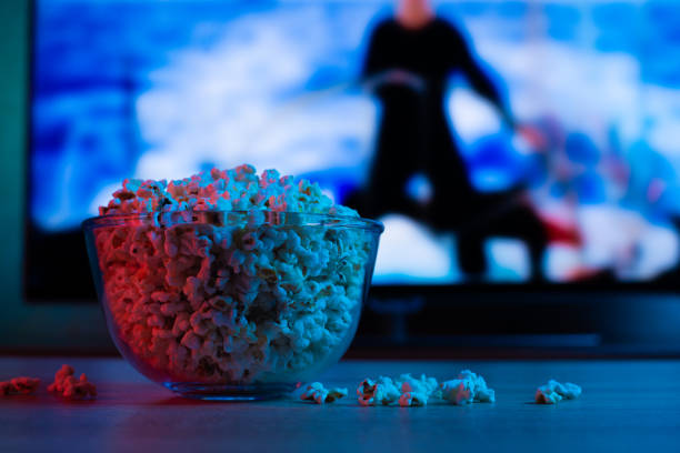popcorn w szklanej płycie na tle telewizora. kolor jasne oświetlenie, niebieski i czerwony. tło - popcorn snack bowl corn zdjęcia i obrazy z banku zdjęć