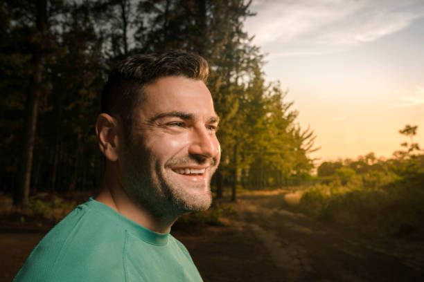 Side view of happy sporty man looking away. Fit male is smiling in forest. He is exercising in woodland.