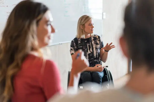 Confident disabled businesswoman giving presentation in office. Focus is on creative female professional. Manager is in meeting with executives at workplace.