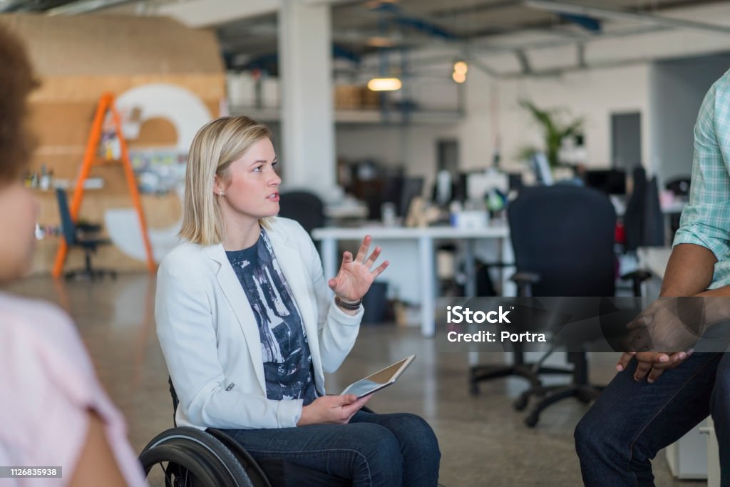 Behinderte Geschäftsfrau diskutiert mit Kollegen - Lizenzfrei Rollstuhl Stock-Foto