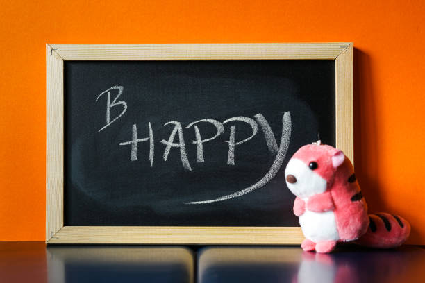 Black board with text B Happy written on chalk and a pink soft toy next to it