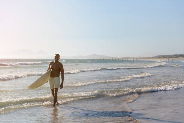 istock Happy man with surfboard walking on shore at beach 1126838729