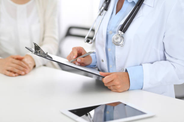 istock Unknown doctor and  female patient  discussing something while standing near reception desk in emergency hospital. Physician at work in clinic. Medicine and health care concept 1126839759