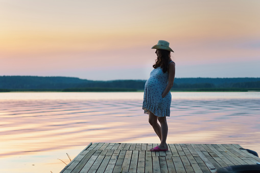 pregnant woman standing on pier near the water on sunset sky backgrounds