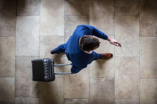 Businessman on the move High angle view of an unrecognizable Caucasian businessman with a suitcase traveling - in an airport or a hotel. business journey stock pictures, royalty-free photos & images