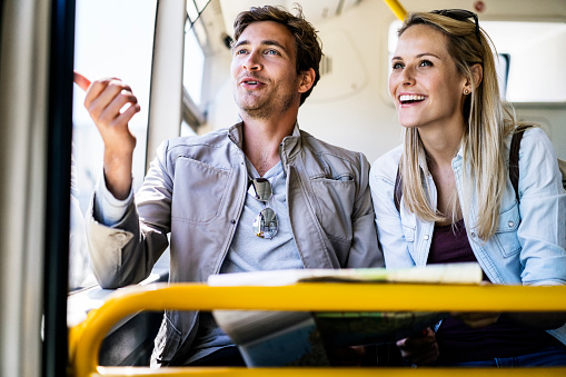 Happy man and woman looking through bus window. Young couple enjoying vacations. Boyfriend showing something to girlfriend in vehicle.