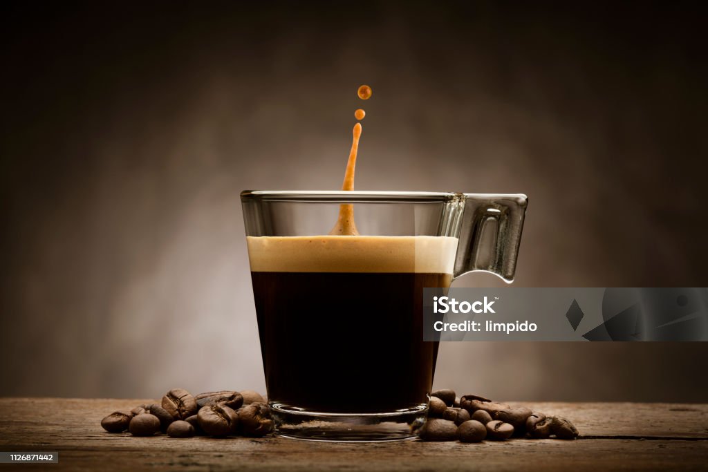 coffee cup Black coffee in glass cup with coffee beans and jumping drop, on wooden table Coffee - Drink Stock Photo
