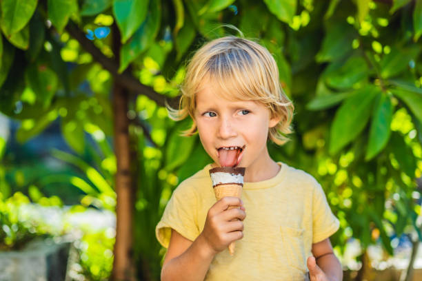 outdoor portrait fröhlicher junge mit eis in waffeln kegel. nettes kind halten eis und fröhlichkeit gesicht bei einem spaziergang im park machen - child chocolate ice cream human mouth stock-fotos und bilder