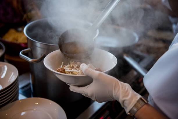 Chef cooking noodle with shrimp and fish ball in local restaurant, Thailand street food. making noodle in Traditional Asian Food. Chinese noodle ripen and ball with spoon in hot soup cocinar sopa de fideos: mano del chef tailandés vierta sopa de soja agua hirviendo al ramen, tallarines con bolas de pescado en un tazón en el restaurante de la tienda, mercadillo de comida de la thai, hacer tallarines en la tradicional comida de asia.
