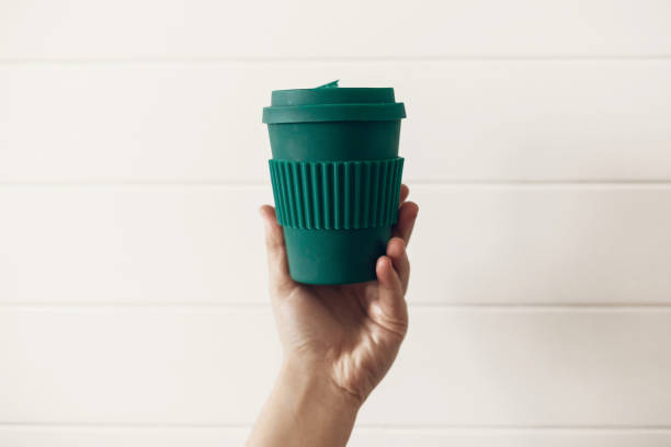 istock Zero waste concept. Hand holding stylish reusable eco coffee cup on white wooden background. Green Cup from natural  bamboo fiber. Ban single use plastic. Make a choice. 1126877276