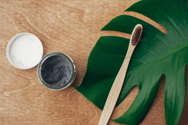 istock Zero waste concept. Natural toothpaste activated charcoal in glass jar and bamboo toothbrush on wooden background with green monstera leaf. Plastic free essentials, teeth care. Sustainable lifestyle 1126877919