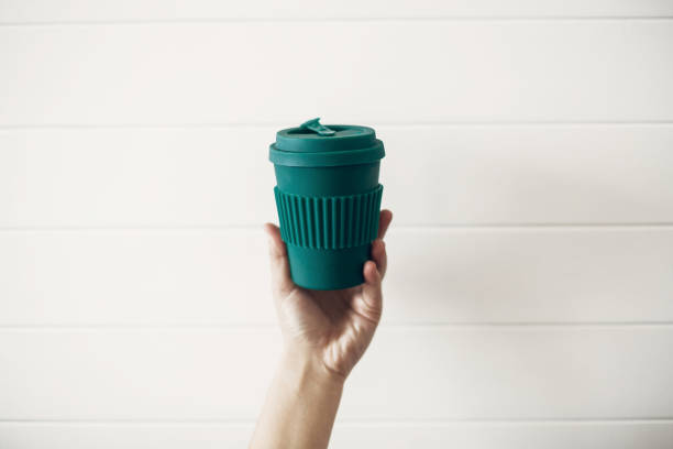 istock Hand holding stylish reusable eco coffee cup on white wooden background. Green Cup from natural  bamboo fiber, zero waste concept. Ban single use plastic. Make a choice. Take away coffee 1126878049