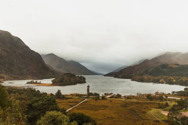 View onto Loch Shiel in Glenfinnan near the Glenfinnan Viaduct with Glenfinnan Monument and fog covered mountains during autumn (Scotland, Europe) Glenfinnan, Scotland, United Kingdom, Europe glenfinnan monument stock pictures, royalty-free photos & images