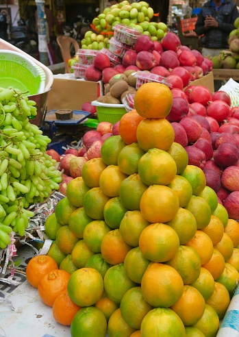 Fresh fruit produce, including, green grapes, red apples, oranges and kiwis, displayed at market stall in India.