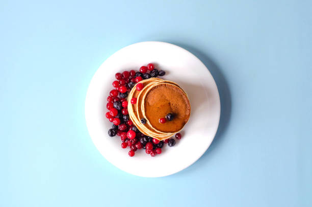 A stack of pancakes with blueberries and cranberries on a white plate on a blue backgrounds.