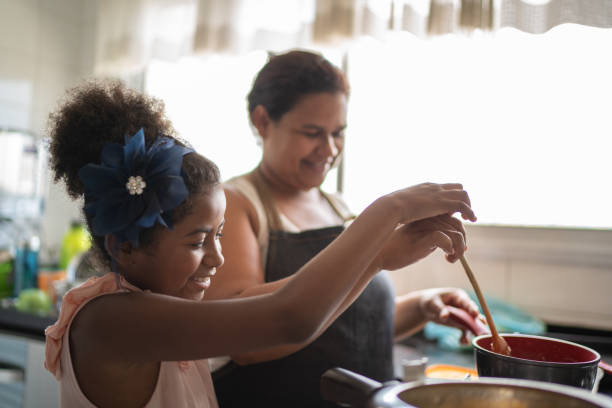 Grandmother cooking with granddaughter, rest of family talks in background