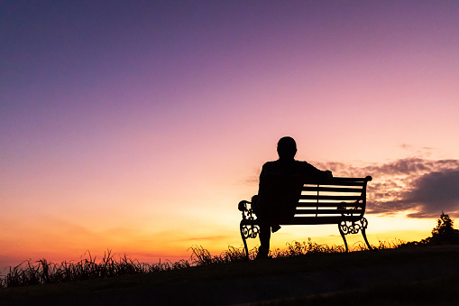 Silhouette of woman sitting alone on the bench against twilight sky over a mountain.