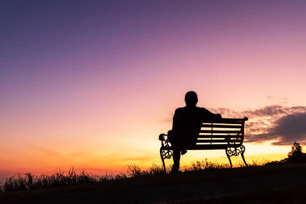 Silhouette of woman sitting alone on the bench against twilight sky over a mountain. stock photo