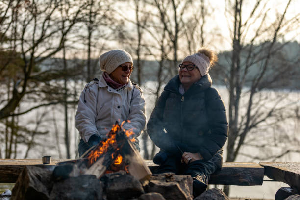 Senior ladies sitting by a bonfire Two senior ladies are sitting on a bench by a burning campfire​ during wintertime. Bonfire stock pictures, royalty-free photos & images