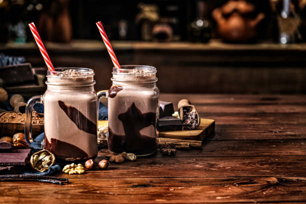 Low key chocolate smoothies on a table in a rustic kitchen Low key chocolate smoothies on a table in a rustic kitchen milkshake photos stock pictures, royalty-free photos & images