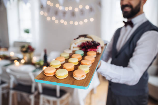 Midsection of man standing indoors in a room set for a party, holding a tray with biscuits.