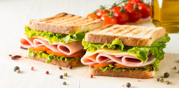 close-up photo of a club sandwich. sandwich with meat, prosciutto, salami, salad, vegetables, lettuce, tomato, onion and mustard on a fresh sliced rye bread on wooden background. olives background. - sandwich club sandwich ham turkey imagens e fotografias de stock