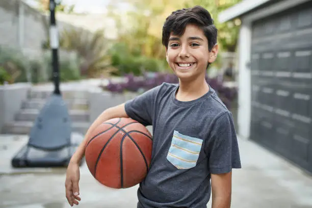 Portrait of smiling boy holding basketball. Happy little male is enjoying weekend. He is wearing casuals in yard.