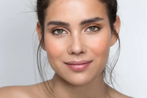 Closeup studio shot of a beautiful teenage girl with freckles skin posing against a grey background