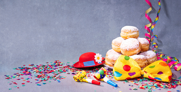 Krapfen, berliner or donuts with bow tie, party hat, streamers and confetti. Colorful carnival or birthday background