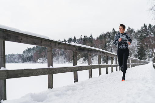 A woman is jogging out in the snow on a cold winter day in Sweden.