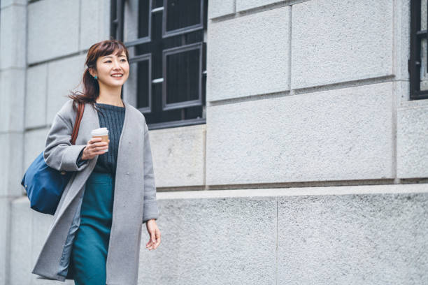 Portrait of businesswoman walking in street while holding coffee A businesswoman is walking in the street while holding a coffee cup. japanese woman stock pictures, royalty-free photos & images