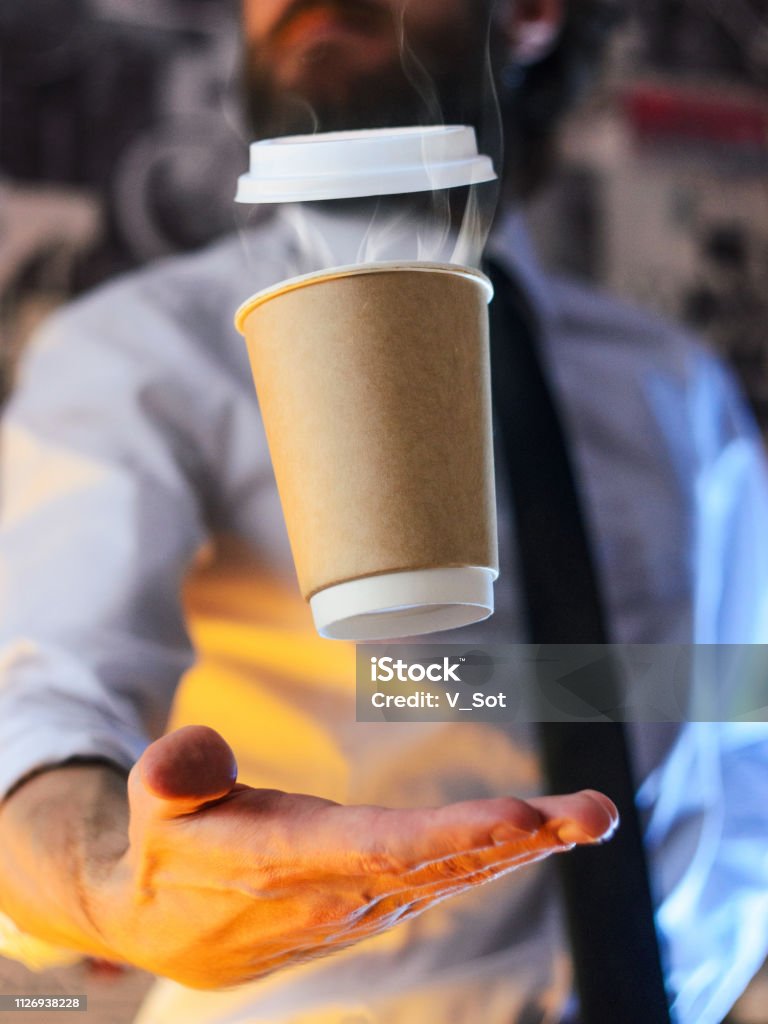 Barista and levitating cup of hot coffee Levitating in the air paper cup with hot coffee. Barista, a bearded young man in a white shirt with a tie, creates miracles - advertises his drink, causing it to soar. Logoplacement concept Adventure Stock Photo